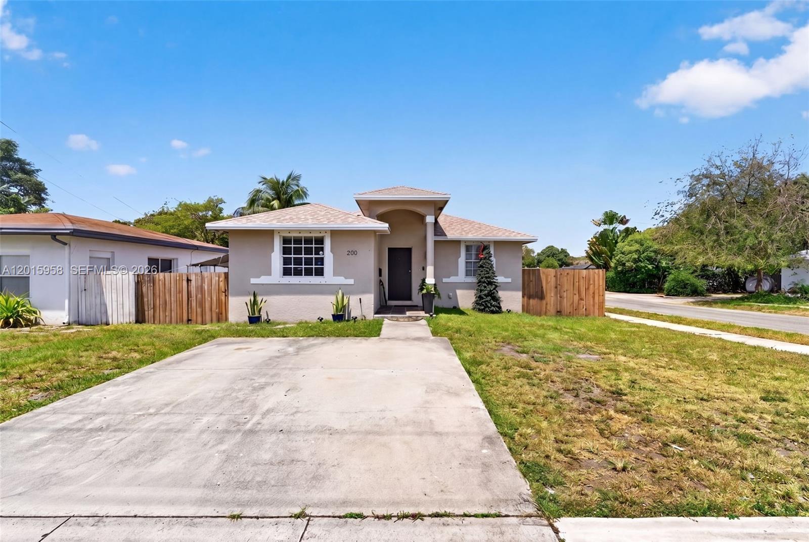 A single-story house with a concrete driveway, tan stucco exterior, and wooden privacy fences — 200 SW 2nd Ave, Hallandale Beach FL 33009, HALLANDALE BEACH, FL