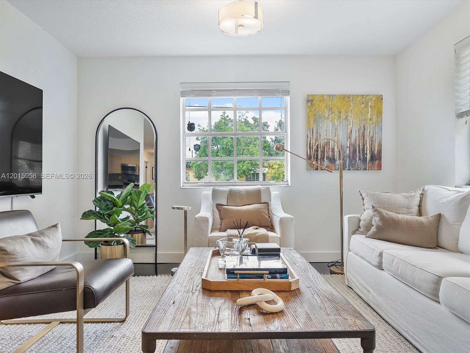 A living room features a wooden coffee table, white sofa, armchair, and a floor mirror — 200 SW 2nd Ave, Hallandale Beach FL 33009, HALLANDALE BEACH, FL