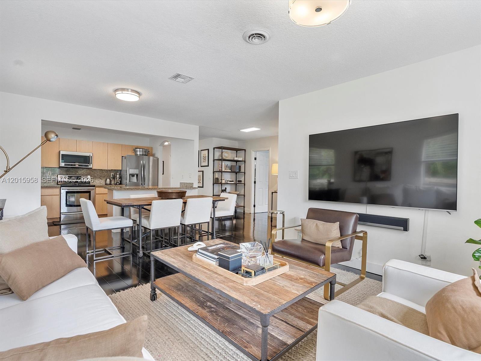 An open-concept living room features a kitchen, dining area, and a large wall-mounted television — 200 SW 2nd Ave, Hallandale Beach FL 33009, HALLANDALE BEACH, FL