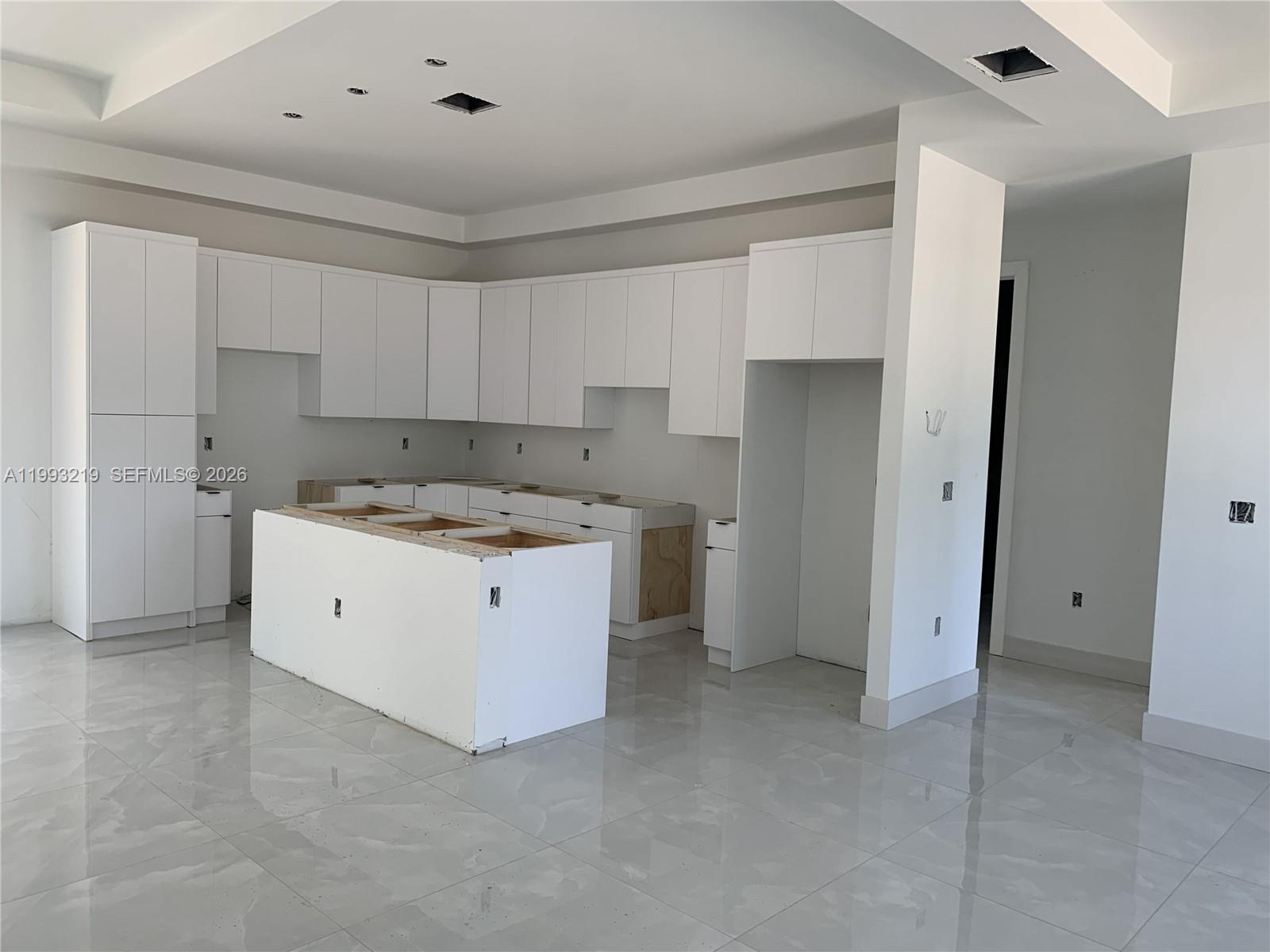 An unfinished kitchen features white cabinets, a central island, and light-colored tile flooring — 1016 Cortez Ave, Lehigh Acres FL 33974, LEHIGH ACRES, FL