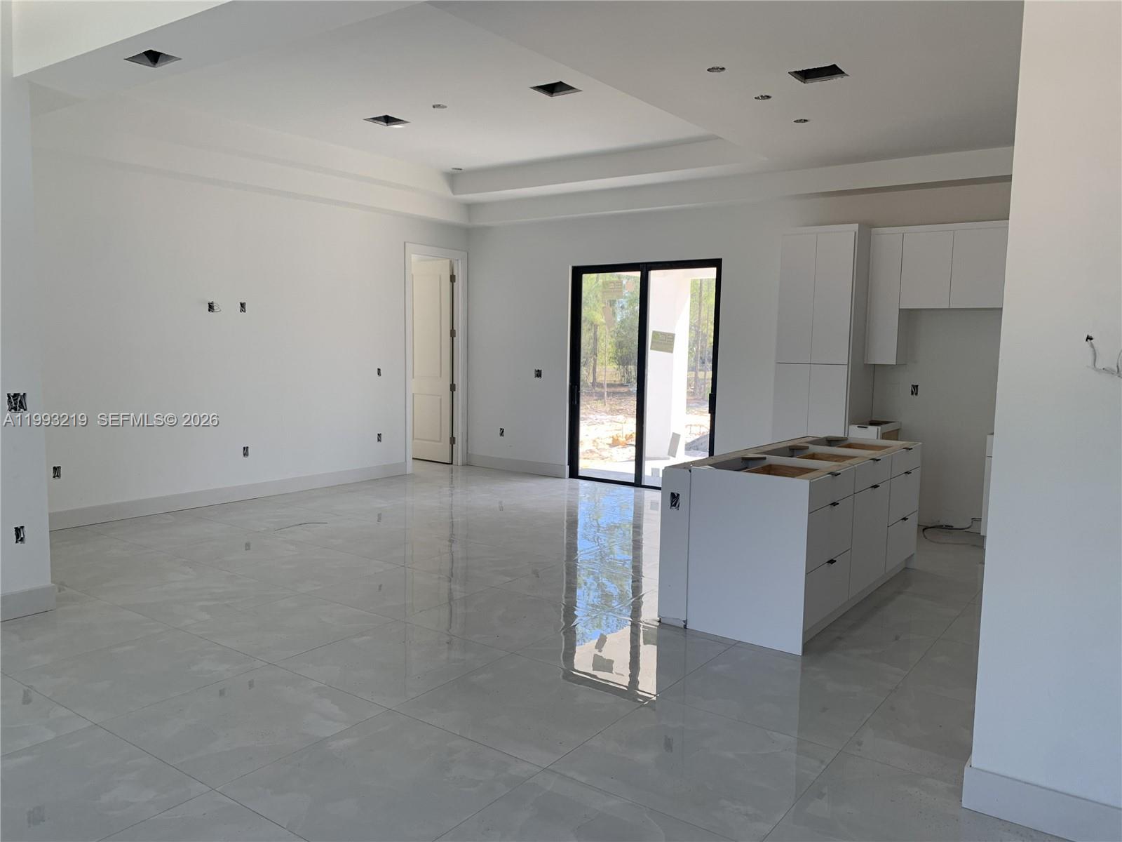 An unfinished kitchen and living area features white cabinetry, a center island, and tiled floors — 1016 Cortez Ave, Lehigh Acres FL 33974, LEHIGH ACRES, FL