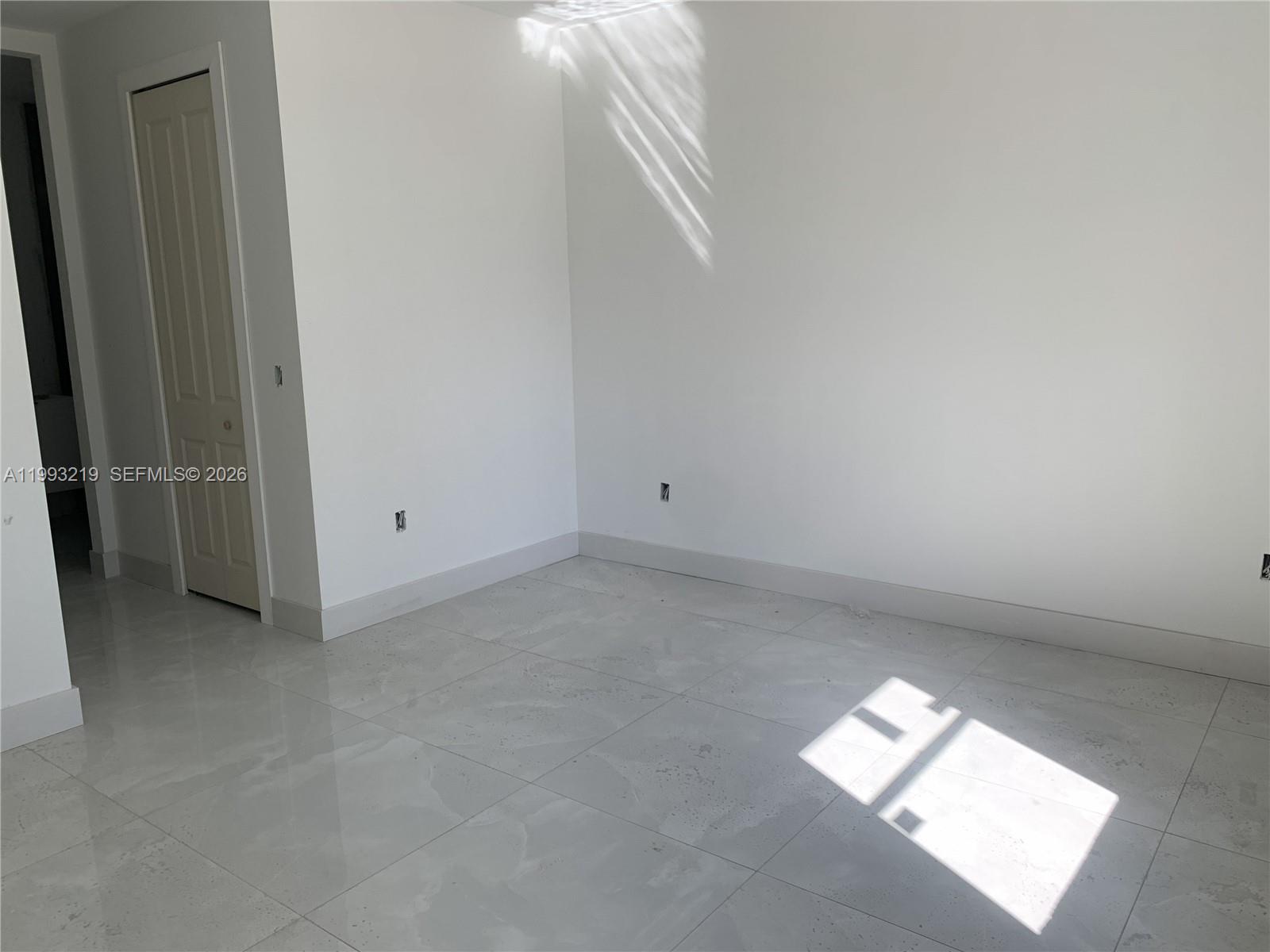 An empty room features white walls, light-colored tile flooring, and a closed interior door — 1016 Cortez Ave, Lehigh Acres FL 33974, LEHIGH ACRES, FL