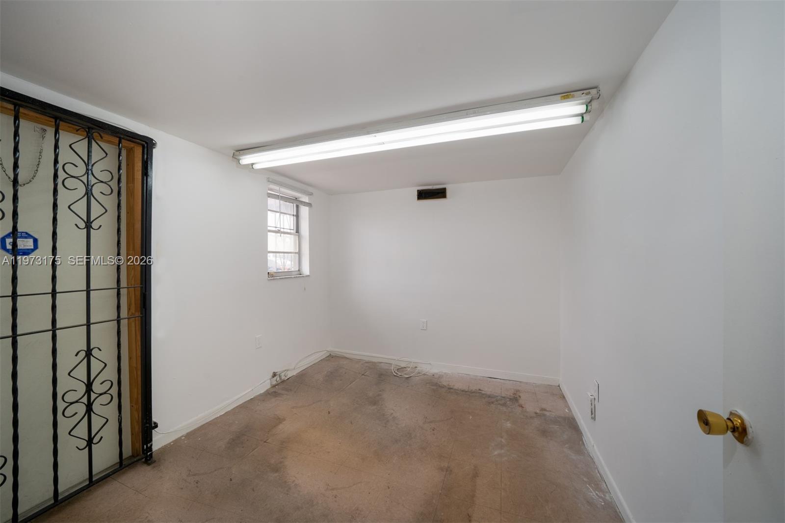 An empty room with white walls, a fluorescent ceiling light, and a metal security door — 1852 NW 20th St # 1852, Miami FL 33142, MIAMI, FL