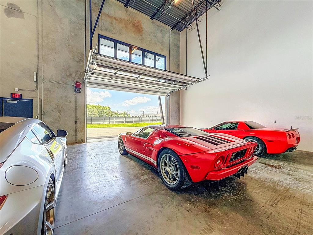 A garage with a large open door, concrete walls, and three parked sports cars — 6500 MOTOR ENCLAVE WAY UNIT #1103, TAMPA, FL