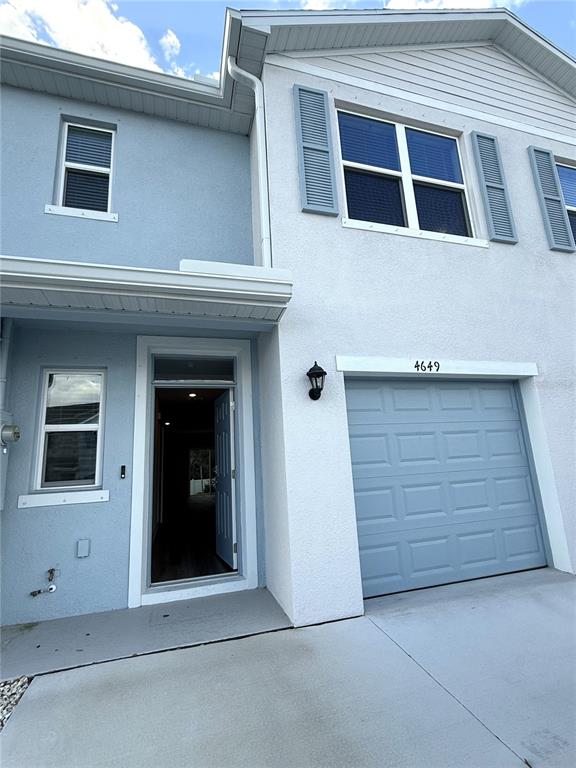 The exterior of a two-story townhouse features light blue stucco, a garage, and an open front door — 4649 PLEASANT AVENUE, PALM HARBOR, FL