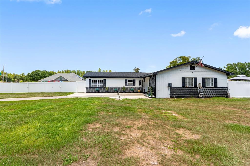 A single-story house with white siding and black brick accents sits behind a white fence — 5515 LAKE LE CLARE ROAD, LUTZ, FL