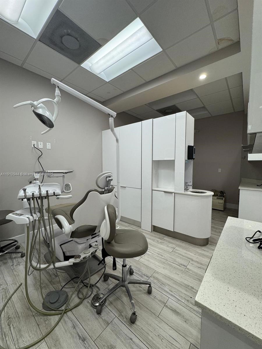 This dental exam room features a patient chair, medical equipment, white cabinetry, and wood-look flooring — 9440 W Commercial Blvd, Sunrise FL 33351, SUNRISE, FL