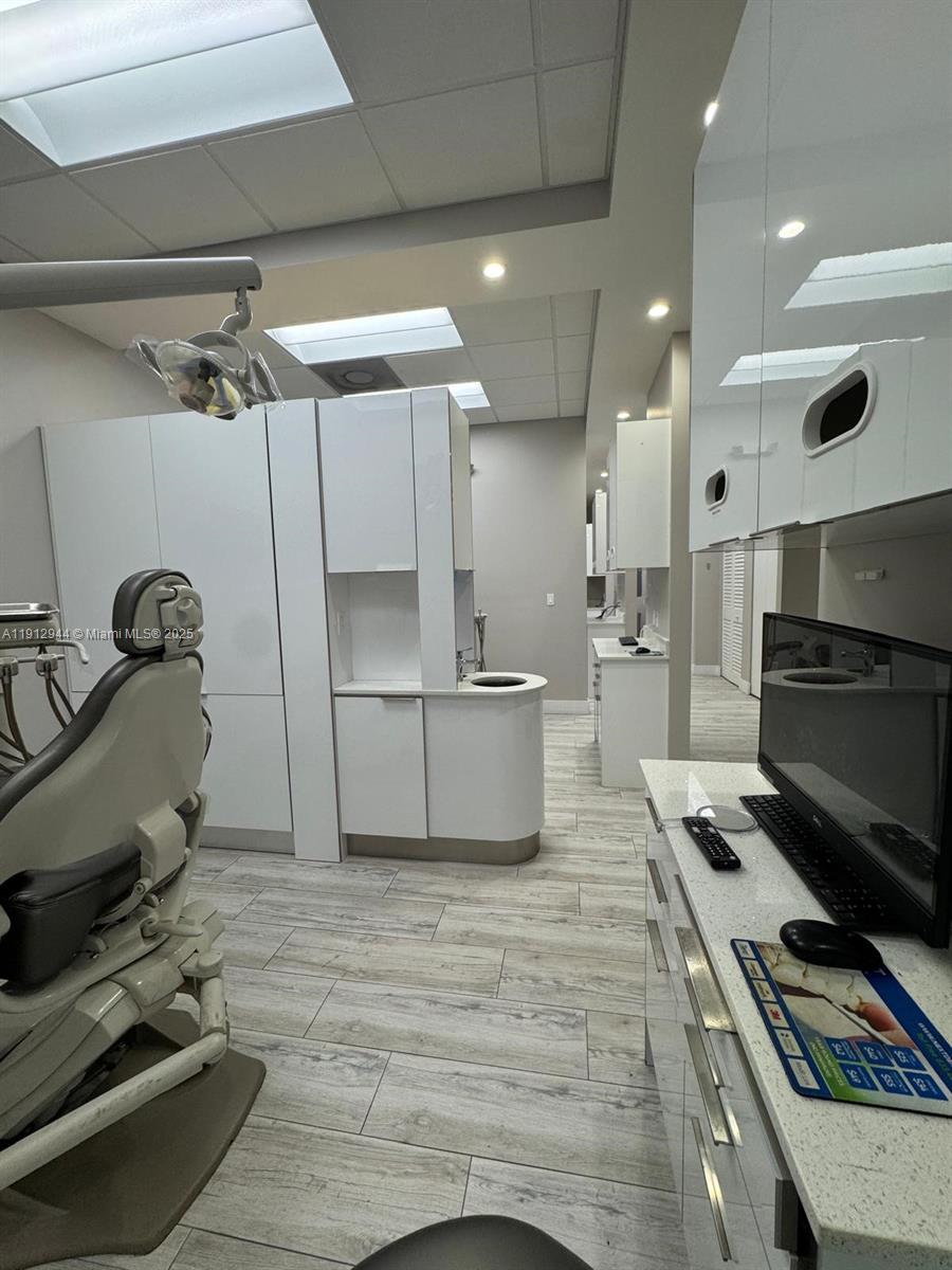 A modern dental examination room features a patient chair, white cabinetry, and wood-look tile flooring — 9440 W Commercial Blvd, Sunrise FL 33351, SUNRISE, FL
