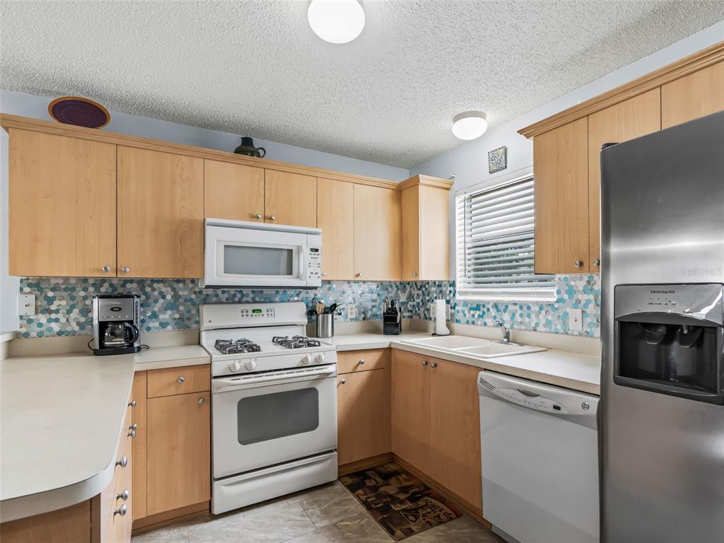 A kitchen with light wood cabinets, stainless steel appliances, and a blue hexagonal tile backsplash — 897 LIVINGSTON LOOP, THE VILLAGES, FL