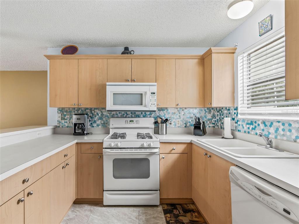 A kitchen features light wood cabinets, white appliances, and a blue and white hexagonal backsplash — 897 LIVINGSTON LOOP, THE VILLAGES, FL