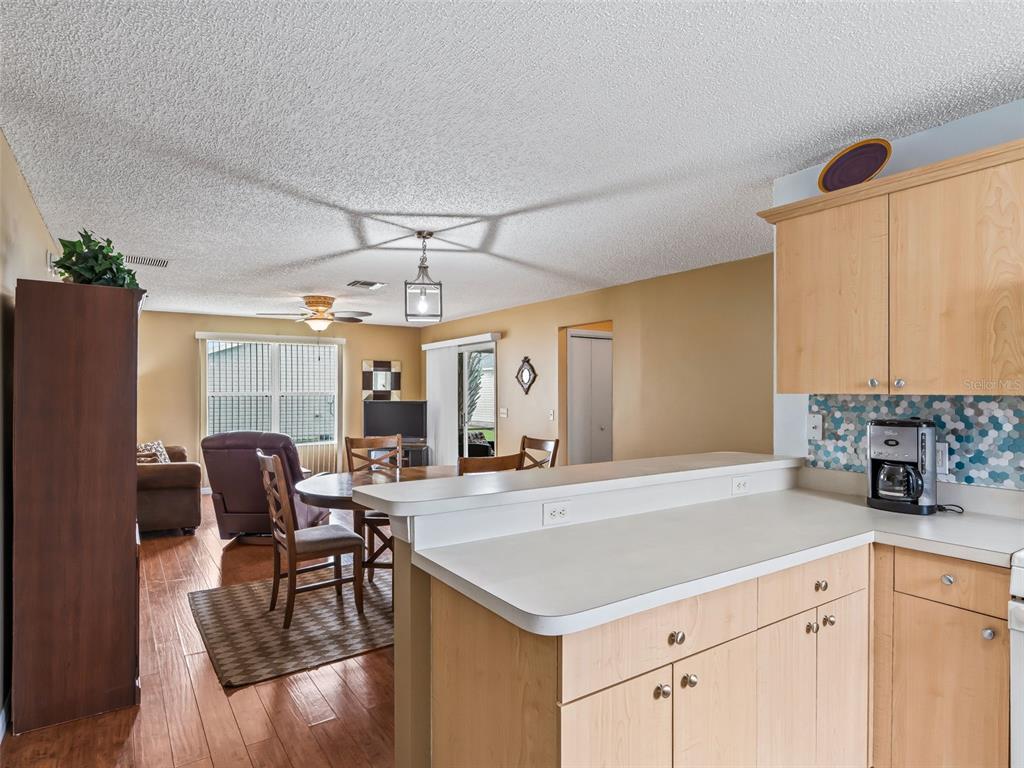 A kitchen with light wood cabinets and a breakfast bar overlooks a dining and living area — 897 LIVINGSTON LOOP, THE VILLAGES, FL