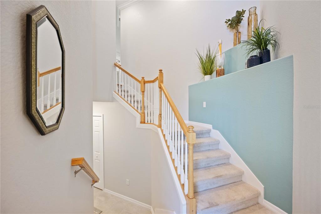 A staircase with light wood railings and carpeted steps features a teal accent wall — 10817 TARFLOWER DRIVE UNIT 201, VENICE, FL