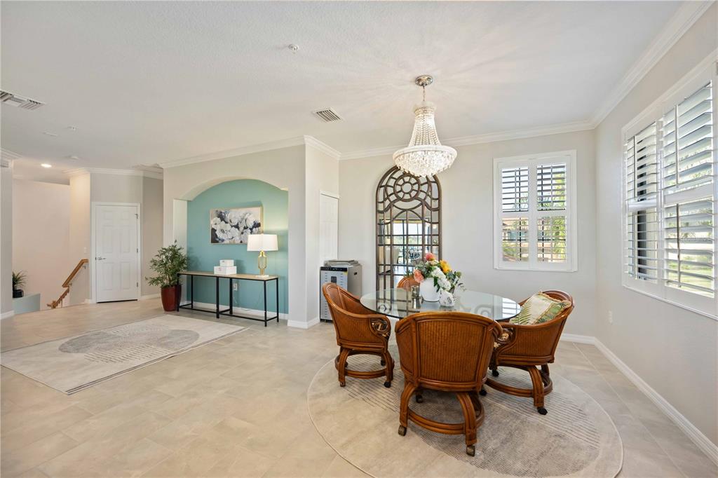 A dining area features a glass table, wicker chairs, a crystal chandelier, and an arched alcove — 10817 TARFLOWER DRIVE UNIT 201, VENICE, FL