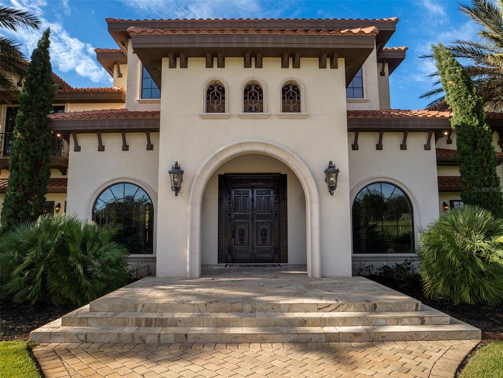 A Mediterranean-style house features a stone entryway with arched double doors and a tiled roof — 9020 SW 9TH STREET ROAD, OCALA, FL