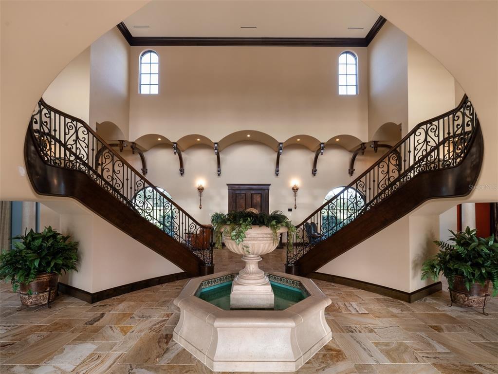 A grand foyer features a central stone fountain, dual curved staircases, and arched wall niches — 9020 SW 9TH STREET ROAD, OCALA, FL