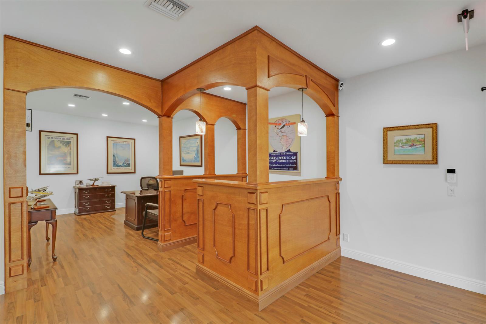 A wood-paneled office partition separates a workspace with a desk and framed vintage travel posters — 725 N Hwy A1a # C110, Jupiter FL 33477, JUPITER, FL