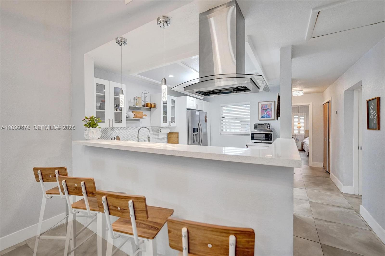 A kitchen features a white breakfast bar, wooden stools, stainless steel appliances, and pendant lighting — 5535 SW 24th Ave, Dania Beach FL 33312, DANIA BEACH, FL