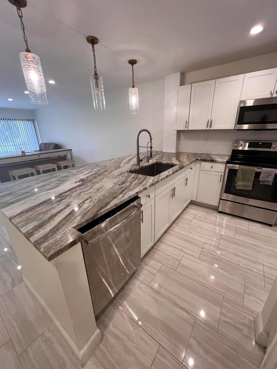 A kitchen with white cabinets, stainless steel appliances, and a large stone-topped island — WEST PALM BEACH, FL