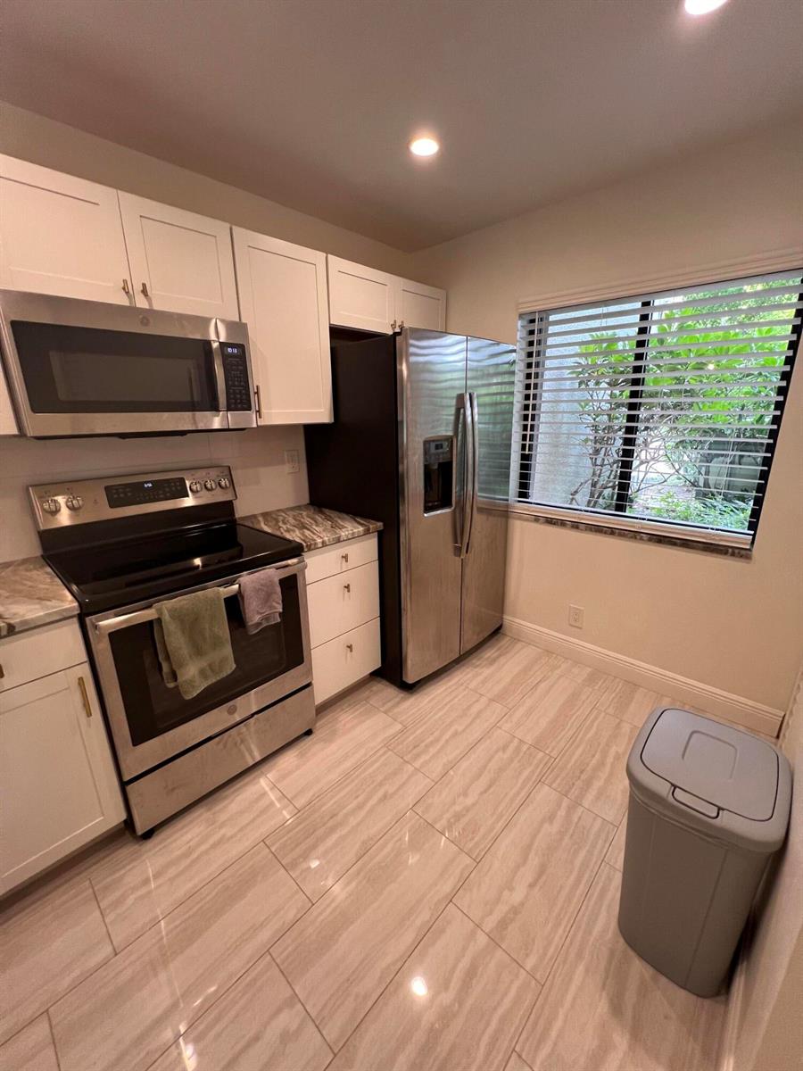A kitchen features white cabinets, stainless steel appliances, marble-patterned countertops, and light-colored tile flooring — WEST PALM BEACH, FL