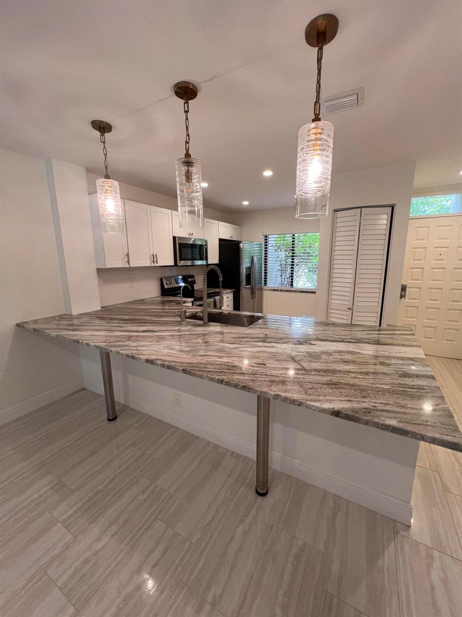 A kitchen features a large stone countertop island with metal supports and three pendant lights — WEST PALM BEACH, FL