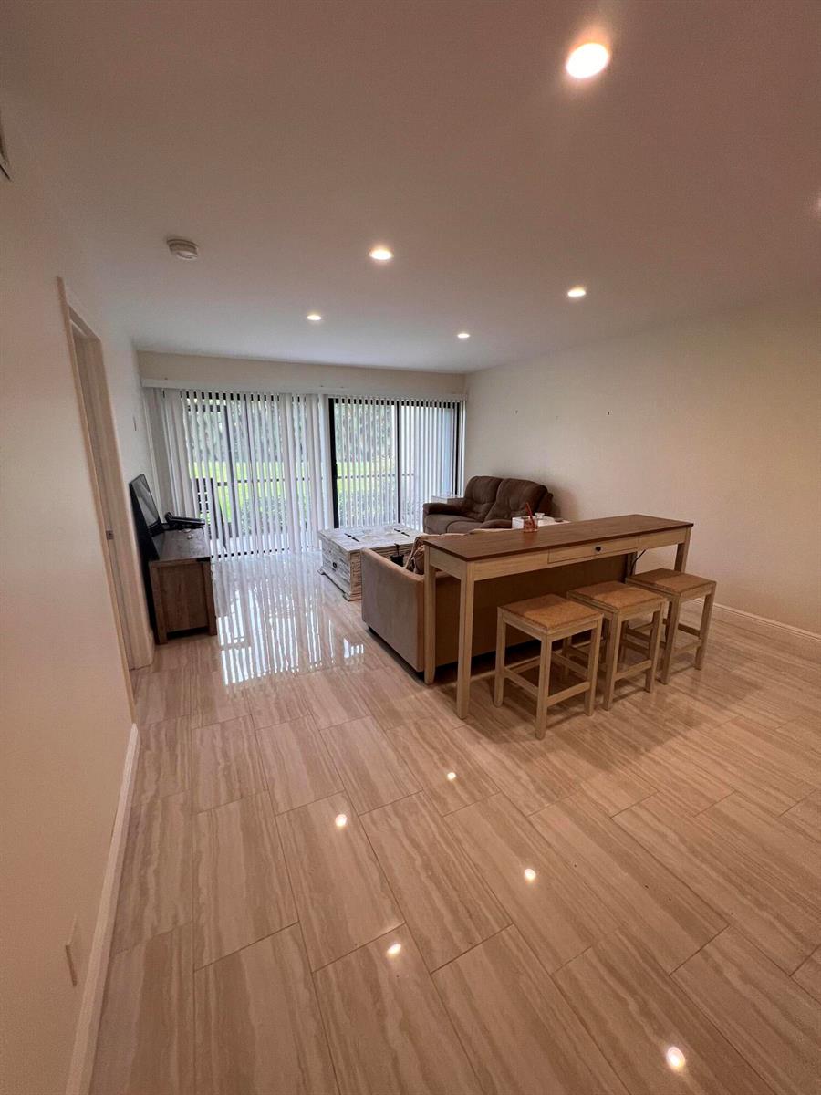 A living room with light-colored tile flooring, a sofa, a console table, and vertical blinds — WEST PALM BEACH, FL