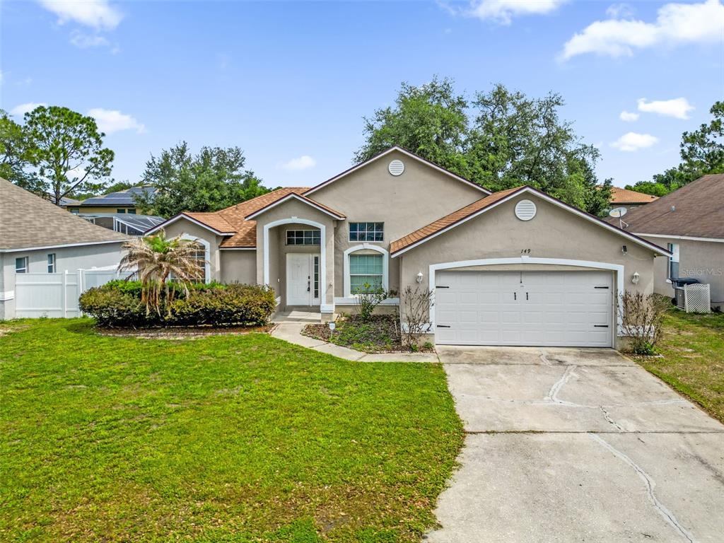 A single-story house with a beige stucco exterior, a two-car garage, and a front lawn — 149 IMPERIAL OAK COURT, DAVENPORT, FL