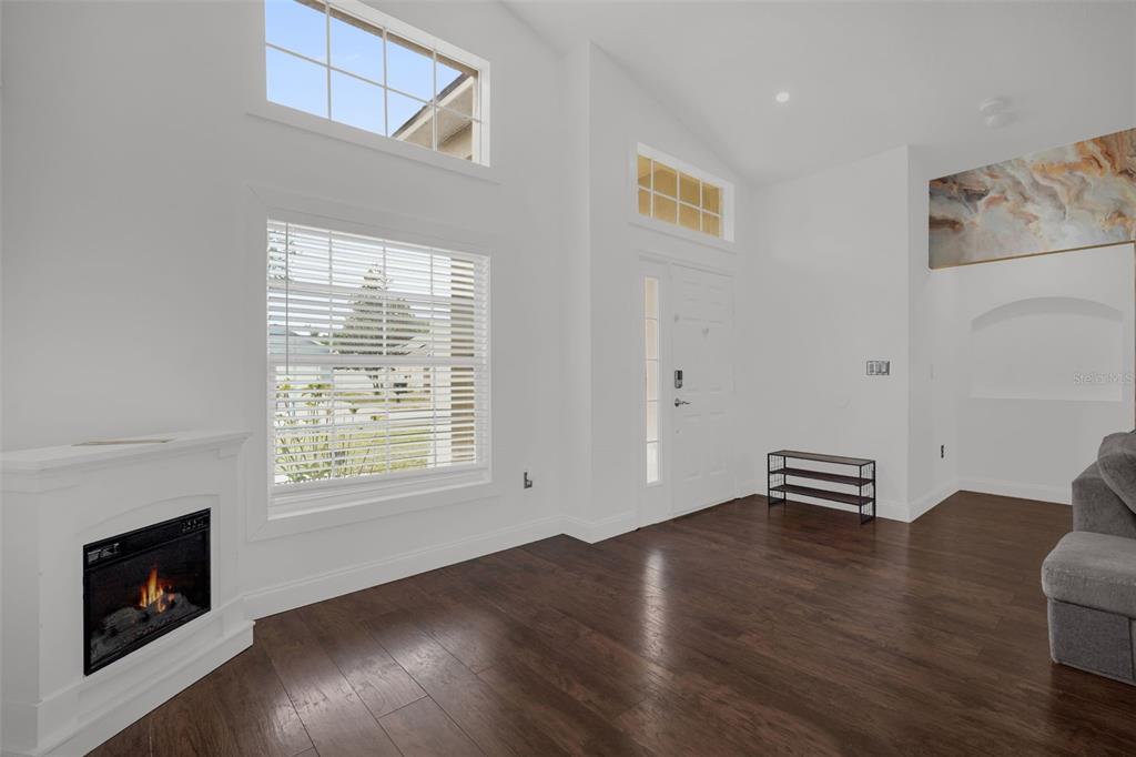 A bright living room features high ceilings, dark wood floors, a fireplace, and large windows — 149 IMPERIAL OAK COURT, DAVENPORT, FL