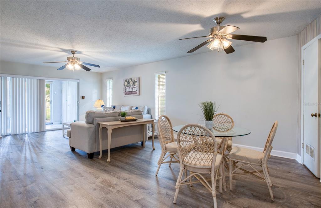 A living and dining area with wood-look flooring, two ceiling fans, and wicker dining chairs — 2206 CORDOVA GREEN, SEMINOLE, FL