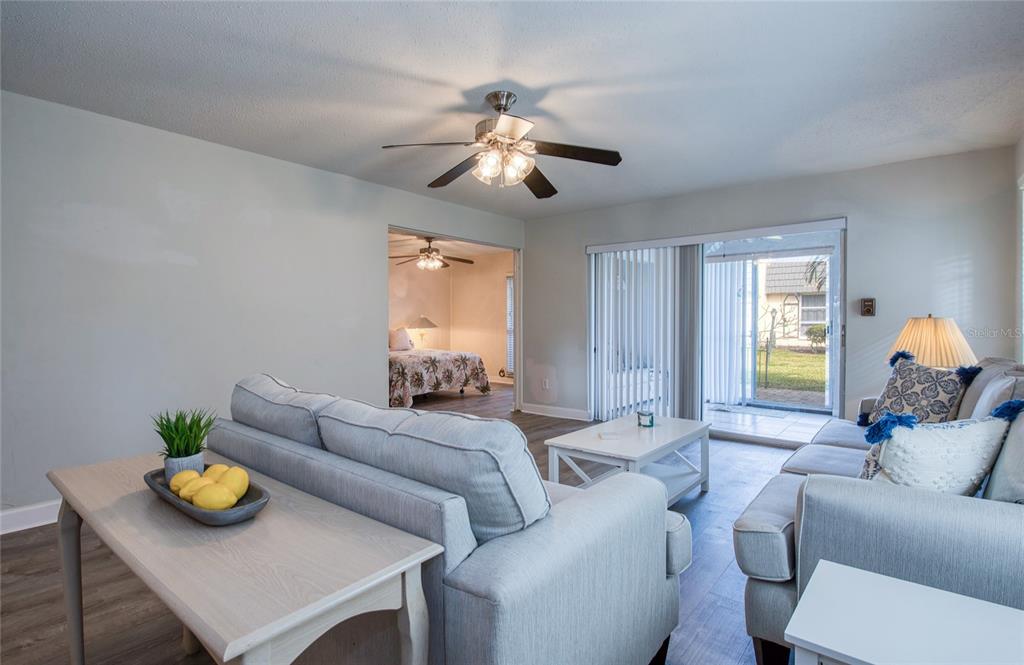 A living room features light-colored furniture, wood-look flooring, a ceiling fan, and sliding glass doors — 2206 CORDOVA GREEN, SEMINOLE, FL