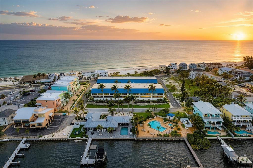 An aerial view shows a coastal neighborhood with houses, a large blue-roofed building, and docks — 1007 GULF DRIVE N UNIT 208, BRADENTON BEACH, FL