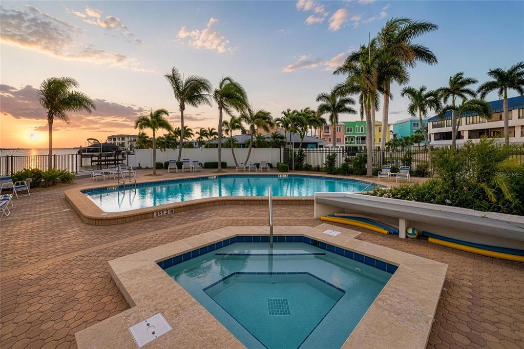 A swimming pool and hot tub on a paved patio overlooking a sunset waterfront view — 1007 GULF DRIVE N UNIT 208, BRADENTON BEACH, FL