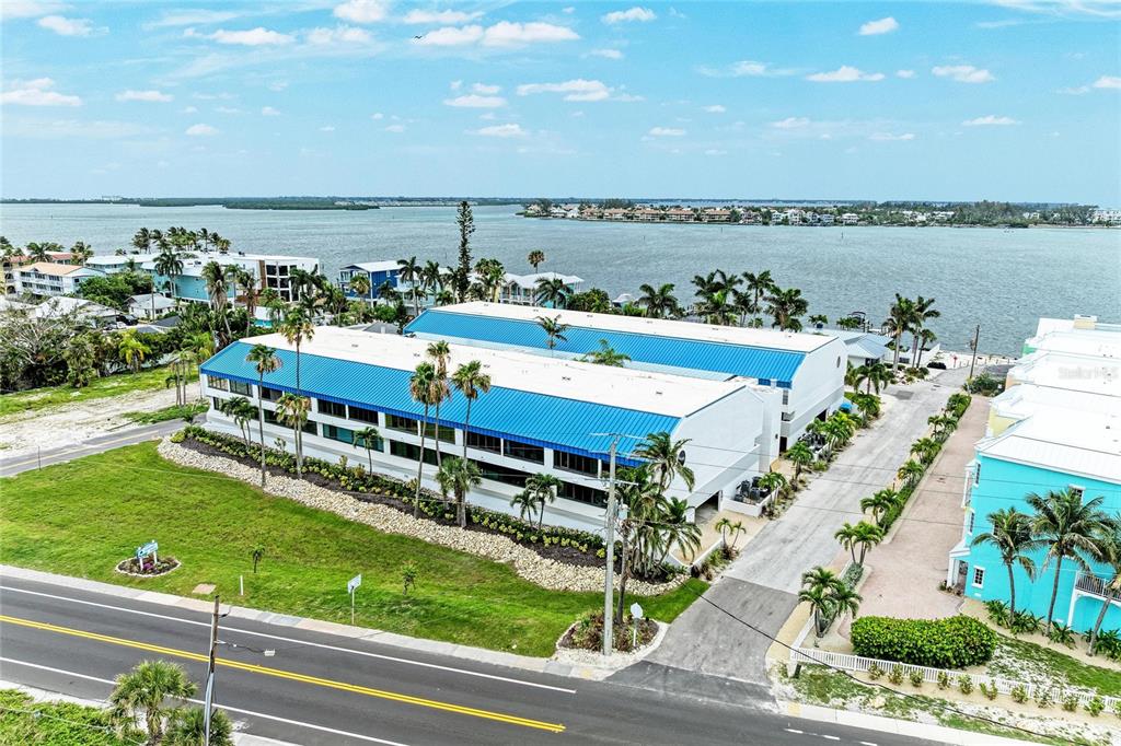 An aerial view shows a multi-story building with a blue roof near a body of water — 1007 GULF DRIVE N UNIT 208, BRADENTON BEACH, FL