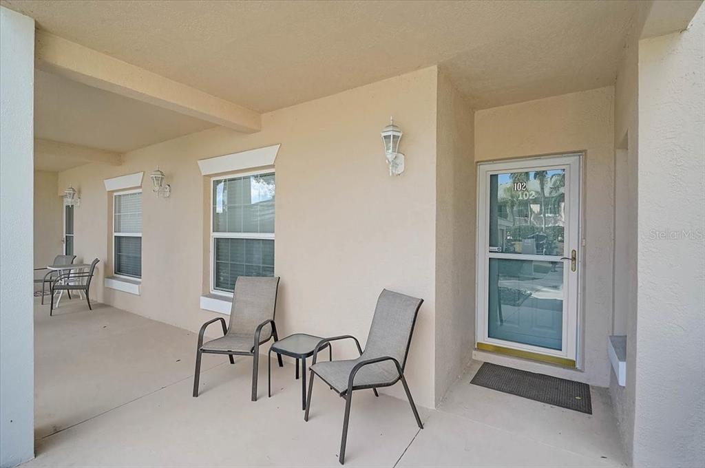 A covered patio features beige stucco walls, two chairs, a small table, and a glass door — 4215 CADDIE DRIVE E UNIT 102, BRADENTON, FL