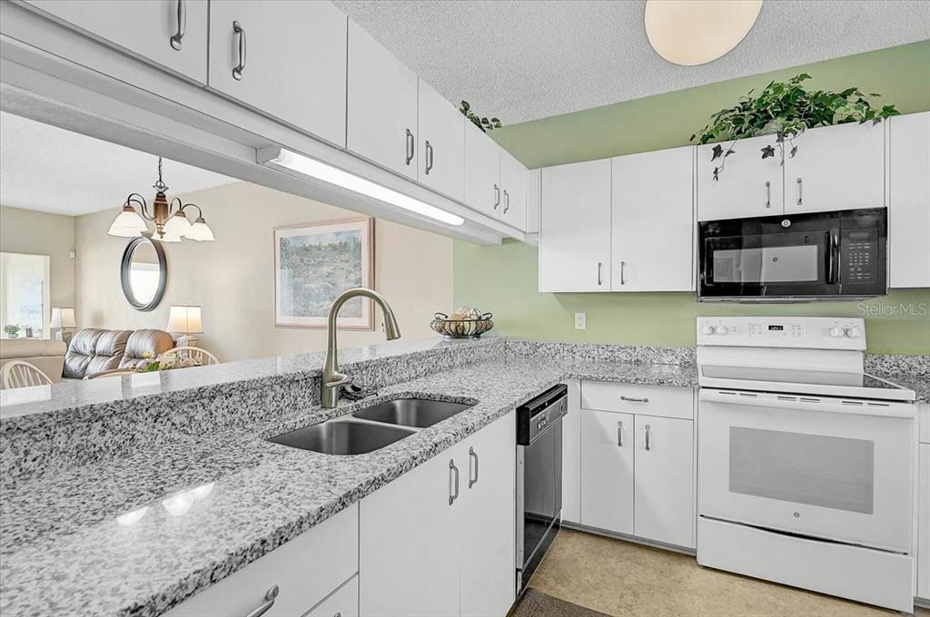 A kitchen with white cabinets, granite countertops, and stainless steel appliances overlooks a living area — 4215 CADDIE DRIVE E UNIT 102, BRADENTON, FL