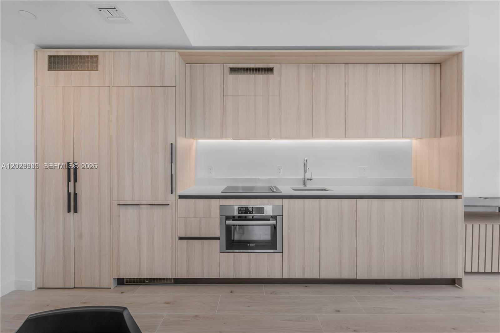 A modern kitchen features light wood cabinetry, integrated appliances, and a white countertop — 225 N Miami # 3109, Miami FL 33128, MIAMI, FL