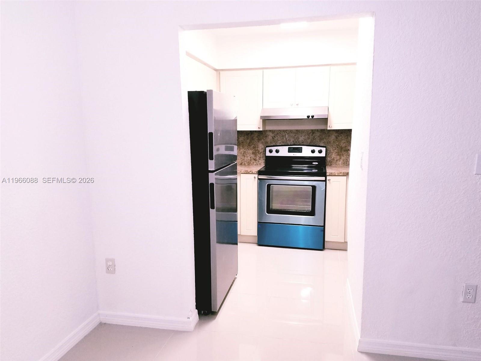 A kitchen features a stainless steel refrigerator, a black electric stove, and white cabinetry — 5748 W 26th Ave # 5748, Hialeah FL 33016, HIALEAH, FL