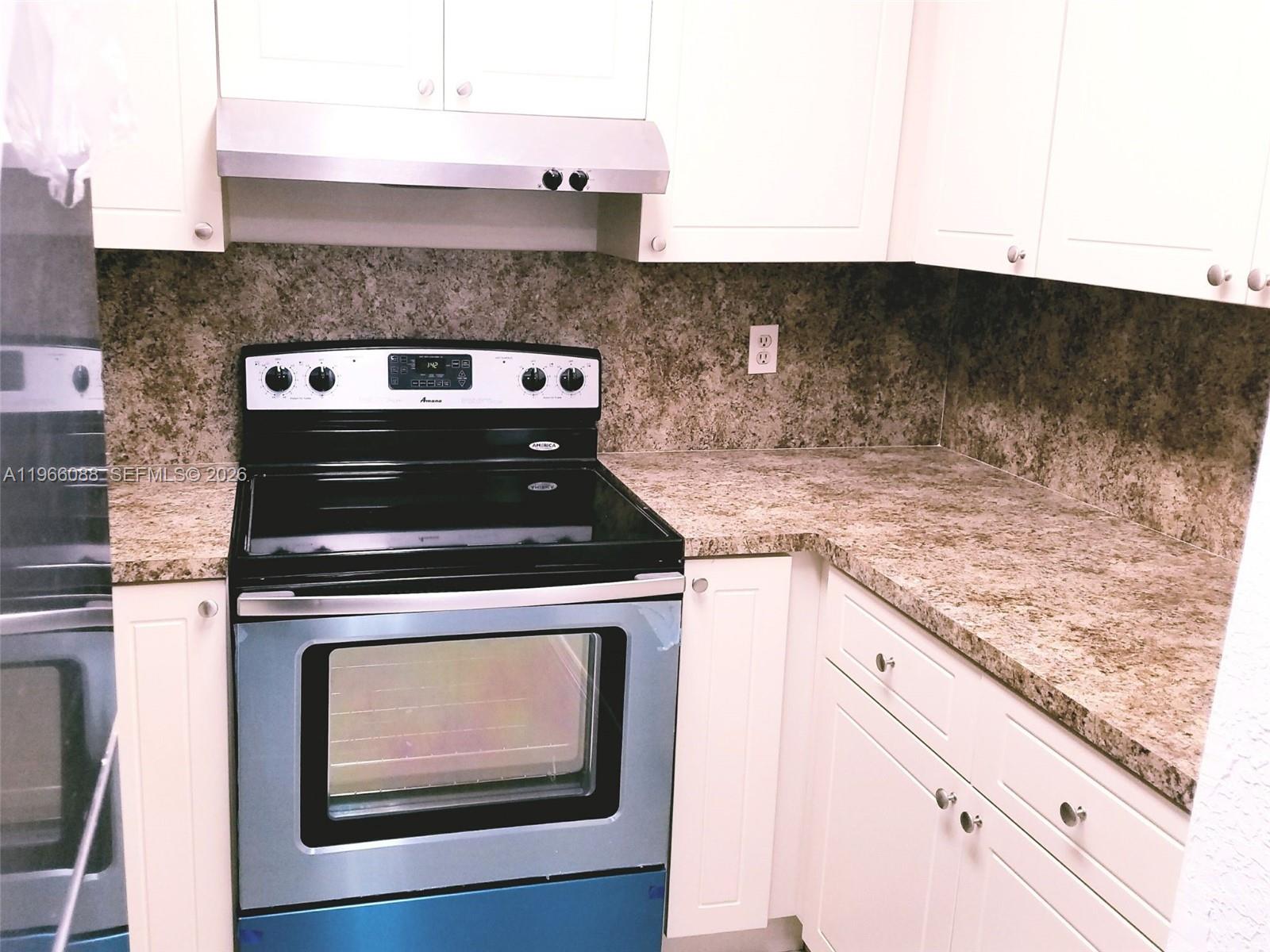 A kitchen features white cabinets, granite countertops, and a black Amana electric range — 5748 W 26th Ave # 5748, Hialeah FL 33016, HIALEAH, FL