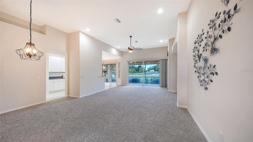 A spacious living room with beige carpet, a ceiling fan, and wall-mounted metal tree decor — 750 BACK NINE DRIVE, VENICE, FL