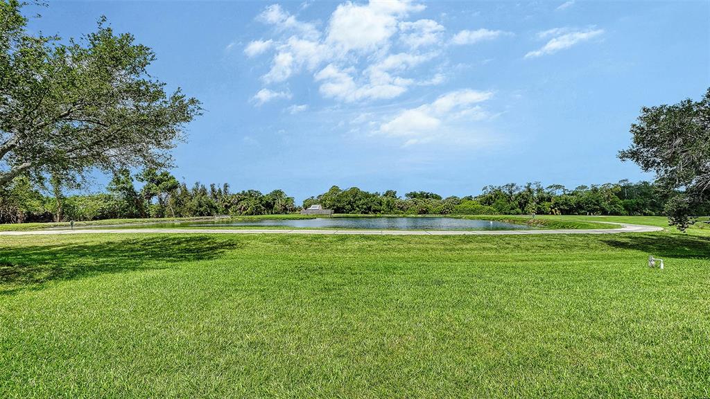 A grassy lawn leads to a pond surrounded by trees under a blue sky — 750 BACK NINE DRIVE, VENICE, FL