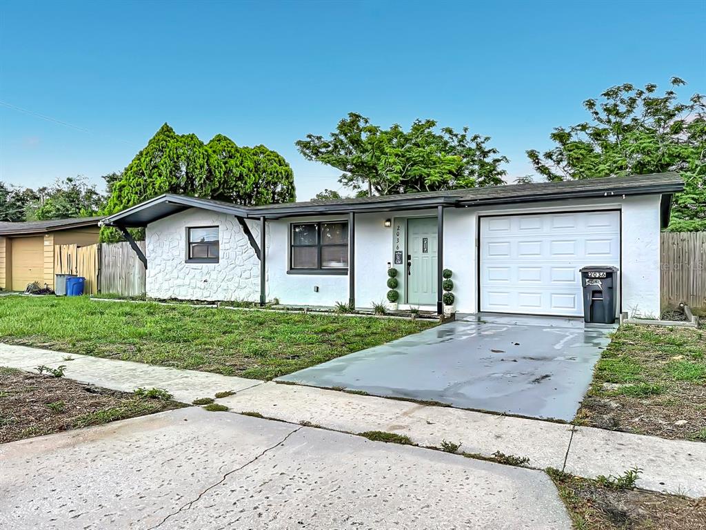A single-story white house with a stone facade, a garage, and a light green door — 2036 SHANNON DRIVE, HOLIDAY, FL