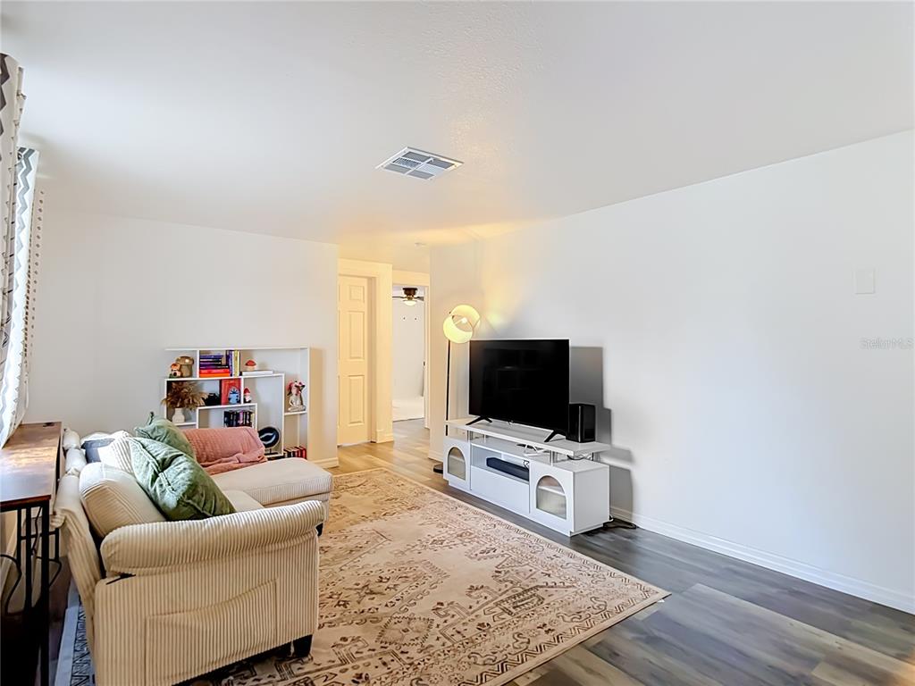 A living room features a sectional sofa, a television on a stand, and wood-look flooring — 2036 SHANNON DRIVE, HOLIDAY, FL