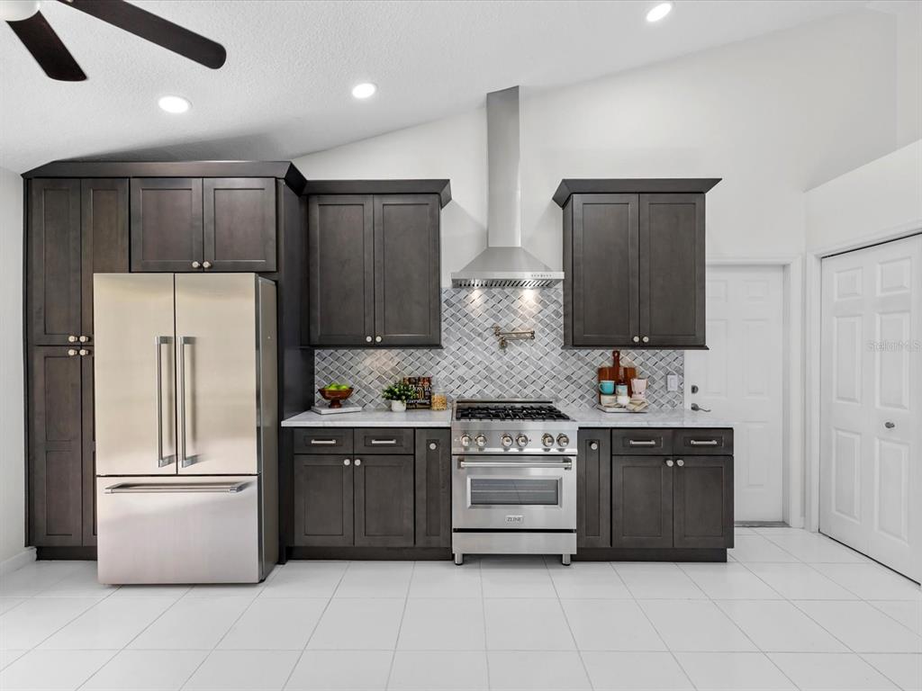 A kitchen features dark wood cabinets, stainless steel appliances, a range hood, and white tile flooring — 9631 OAKWOOD HILLS COURT, NEW PORT RICHEY, FL