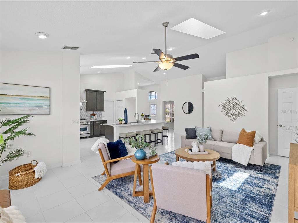 A bright living room with white tile floors, a blue area rug, and an open kitchen — 9631 OAKWOOD HILLS COURT, NEW PORT RICHEY, FL