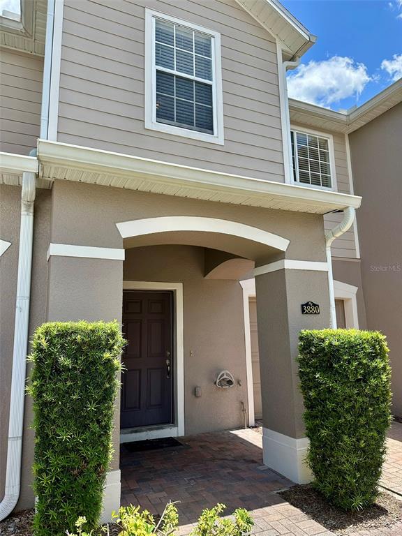 A tan two-story townhouse exterior features a covered entryway, a dark door, and two topiaries — 3880 WHITE BIRCH RUN, WINTER SPRINGS, FL