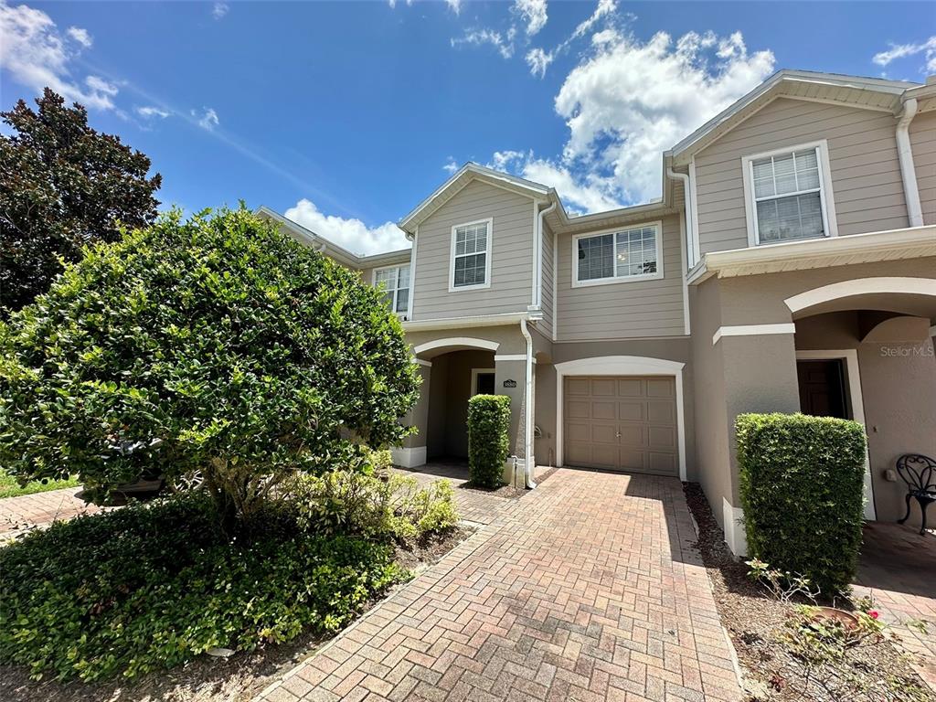 A two-story townhouse exterior features a brick driveway, a single-car garage, and manicured landscaping — 3880 WHITE BIRCH RUN, WINTER SPRINGS, FL