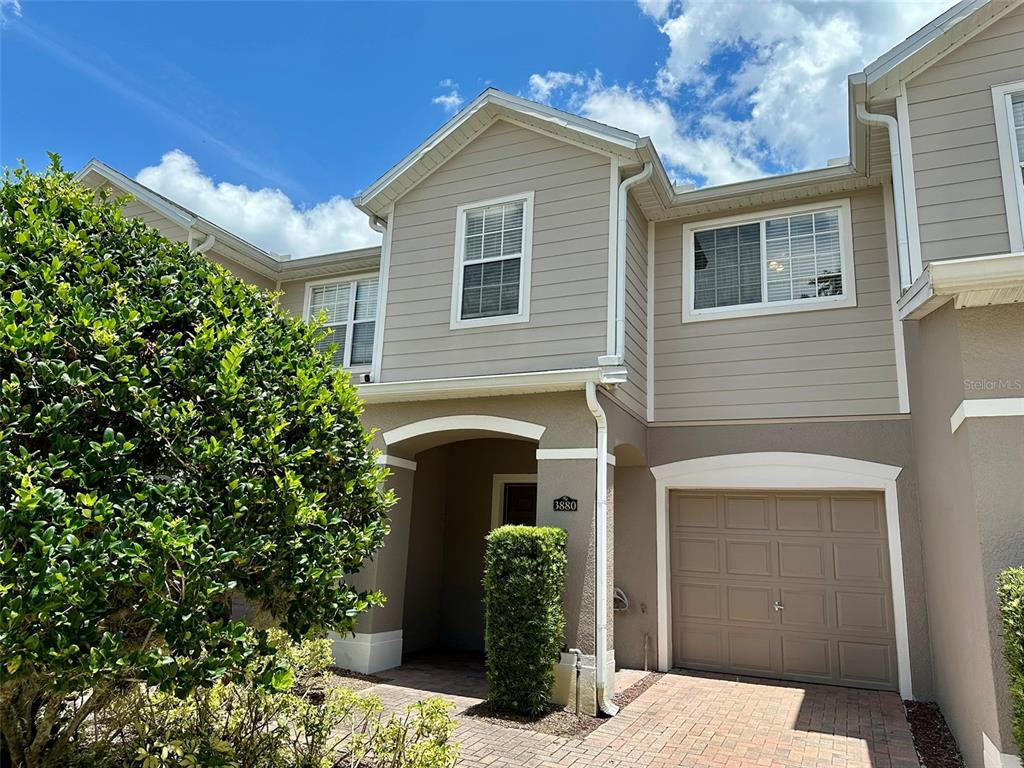 A two-story townhouse exterior features tan siding, a single-car garage, and a paved driveway — 3880 WHITE BIRCH RUN, WINTER SPRINGS, FL