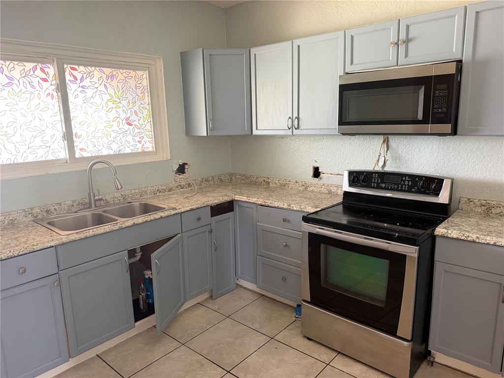 A kitchen features blue cabinets, stainless steel appliances, and speckled laminate countertops — 1204 MICHIGAN AVENUE, ST CLOUD, FL
