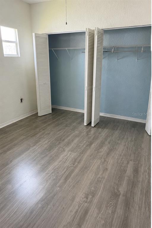 An empty bedroom features light wood-look flooring, white walls, and a large closet with louvered doors — 1204 MICHIGAN AVENUE, ST CLOUD, FL