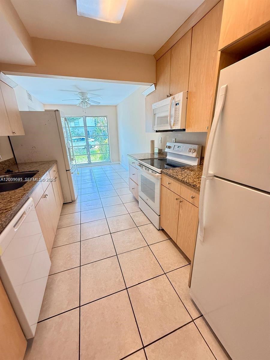 This kitchen features light wood cabinets, granite countertops, white appliances, and light-colored tile flooring — 3301 Raleigh St # 4D, Hollywood FL 33021, HOLLYWOOD, FL