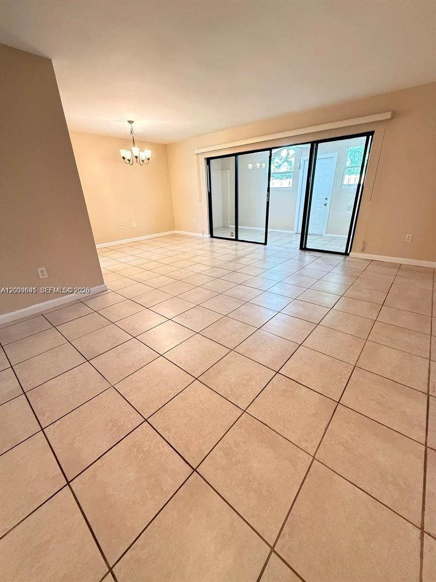 An empty living room features beige tile flooring, a chandelier, and sliding glass patio doors — 3301 Raleigh St # 4D, Hollywood FL 33021, HOLLYWOOD, FL